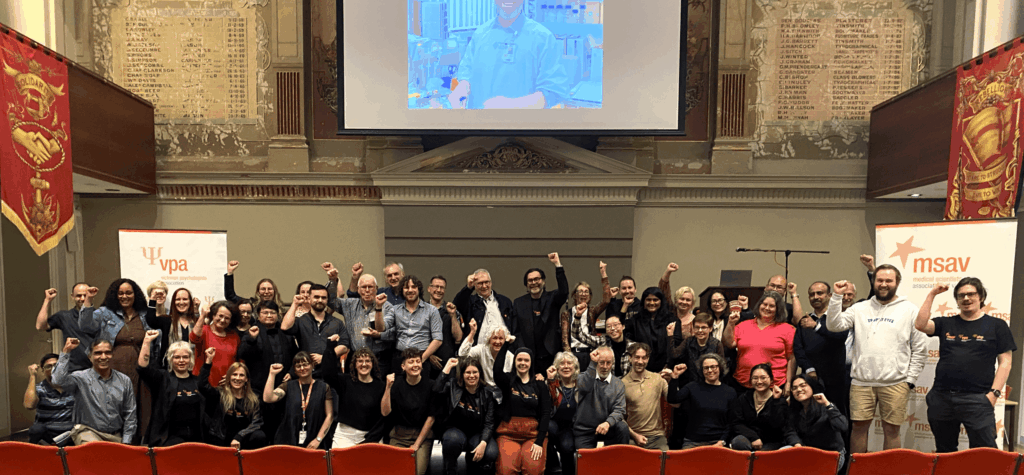 A large gathering of union members posing in a large group with several people holding their arms aloft.